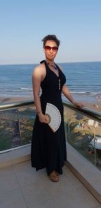 Birgit Ligotzky im schwarzen Kleid vor dem Meer auf einem Balkon